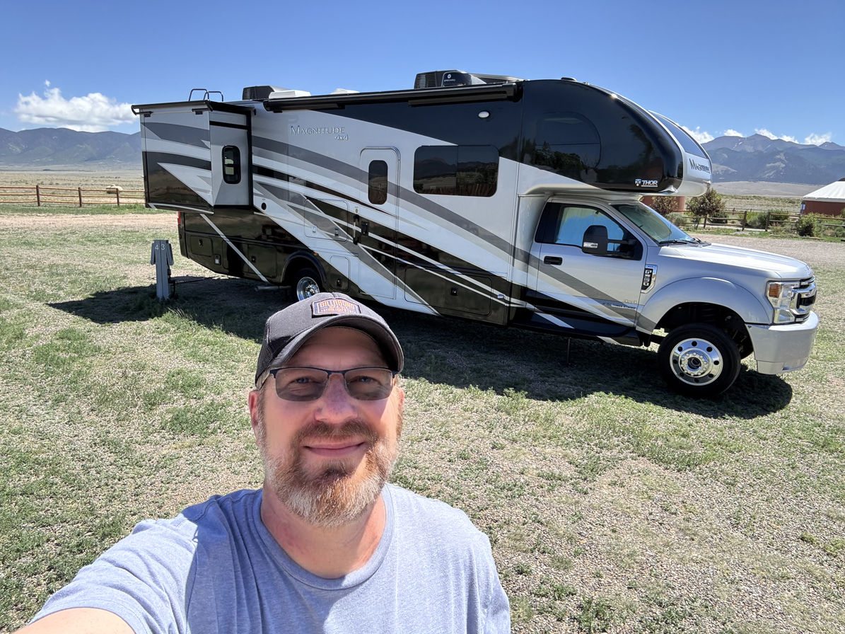 Joe standing in front of his Thor Magnitude super-C RV in a mountain valley